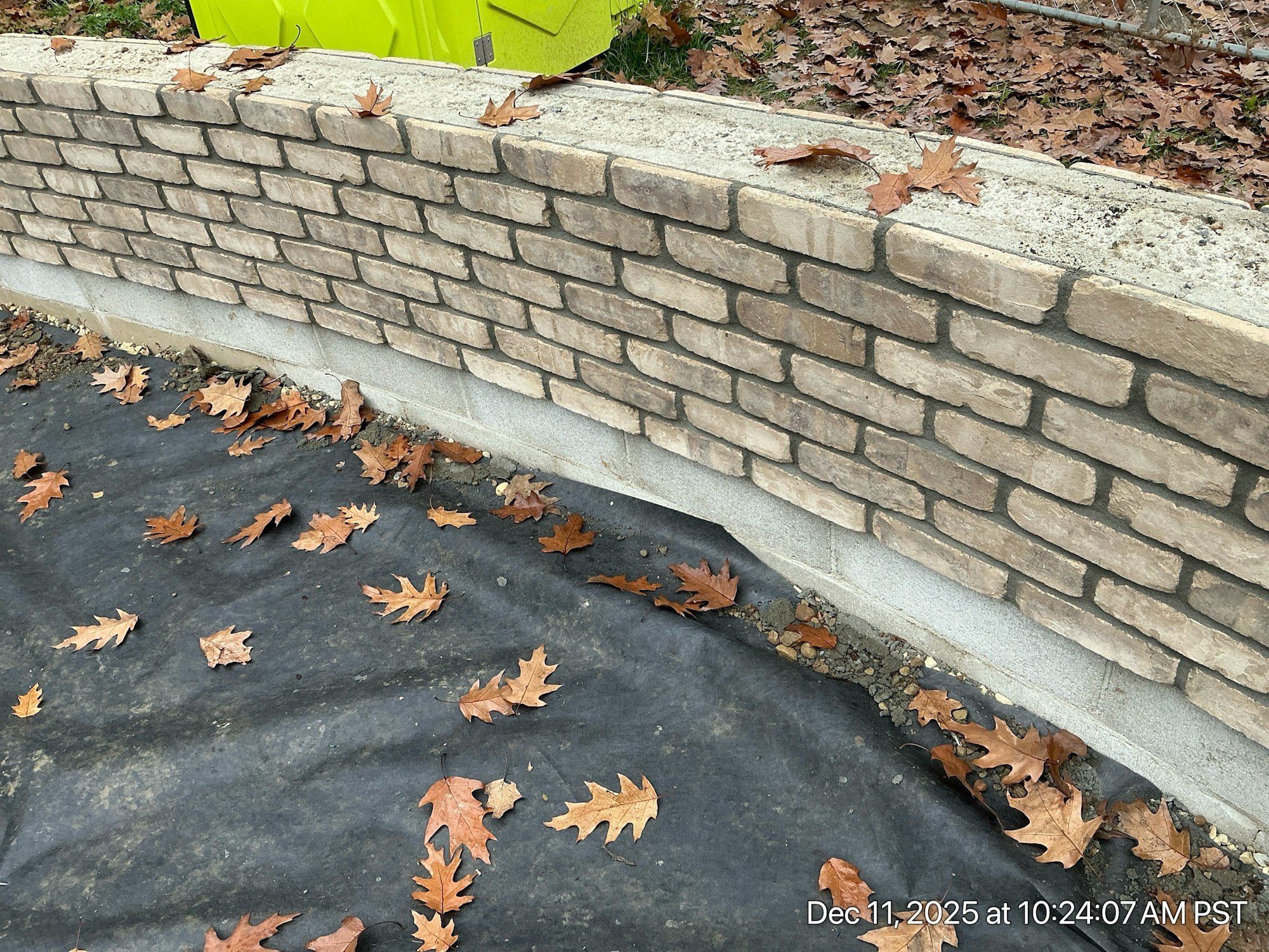 The image shows a stone wall with autumn leaves scattered on a dark surface, indicating a possible outdoor construction area.