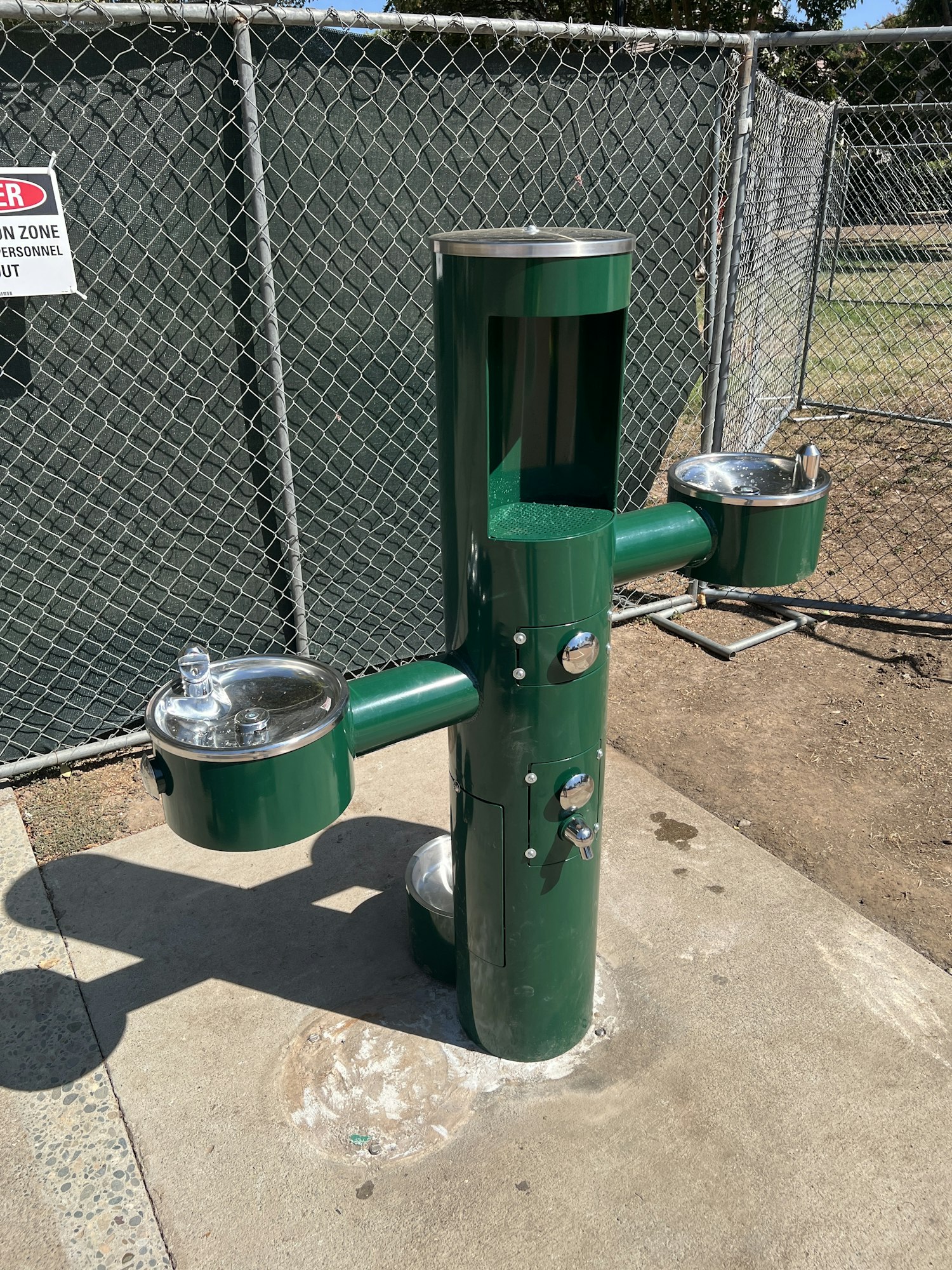 A green outdoor drinking fountain setup with two spouts and a bottle-filling station.