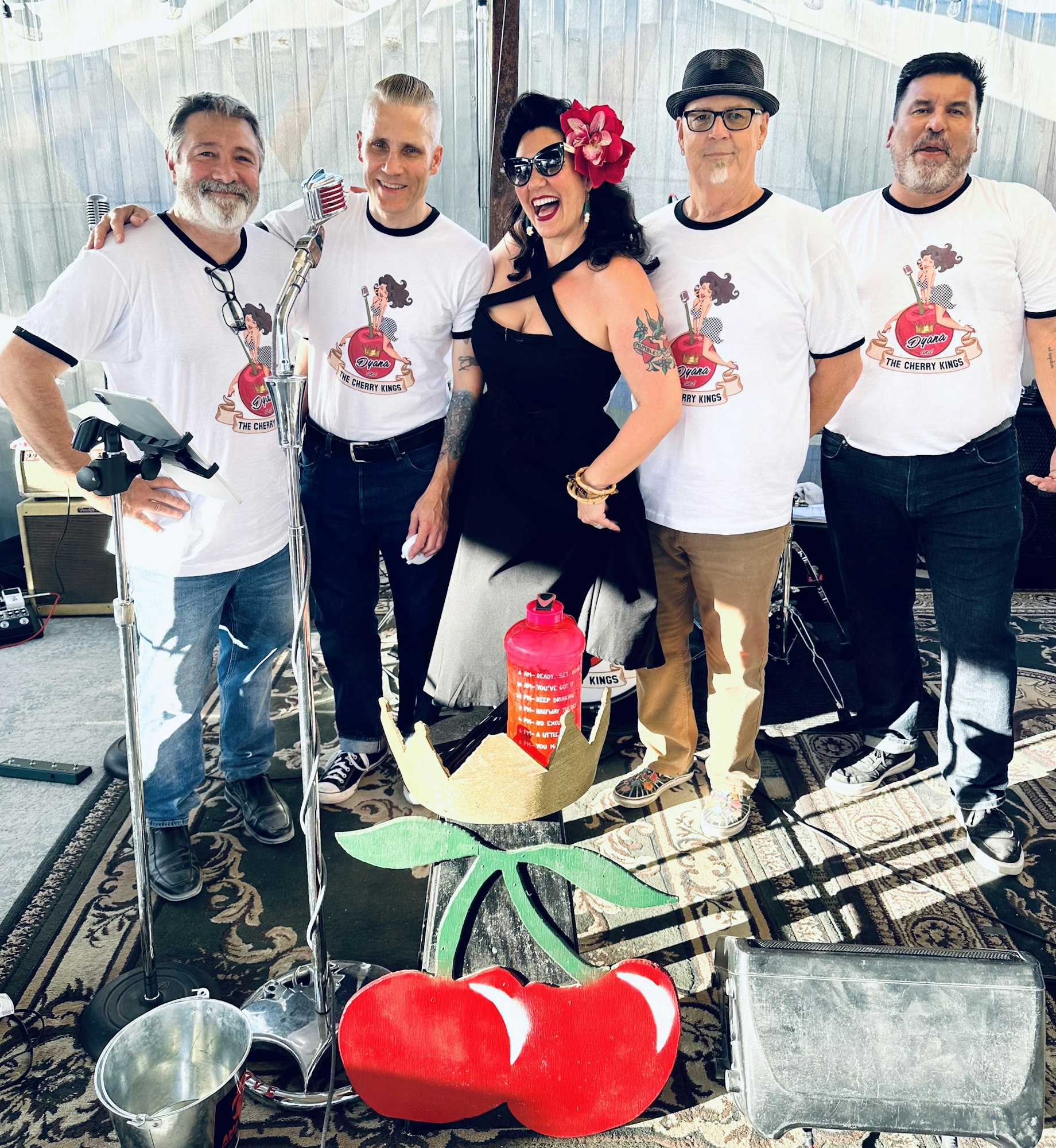 A group of people posing with a microphone and cherry-themed props. They're wearing matching "Cherry Kings" shirts.