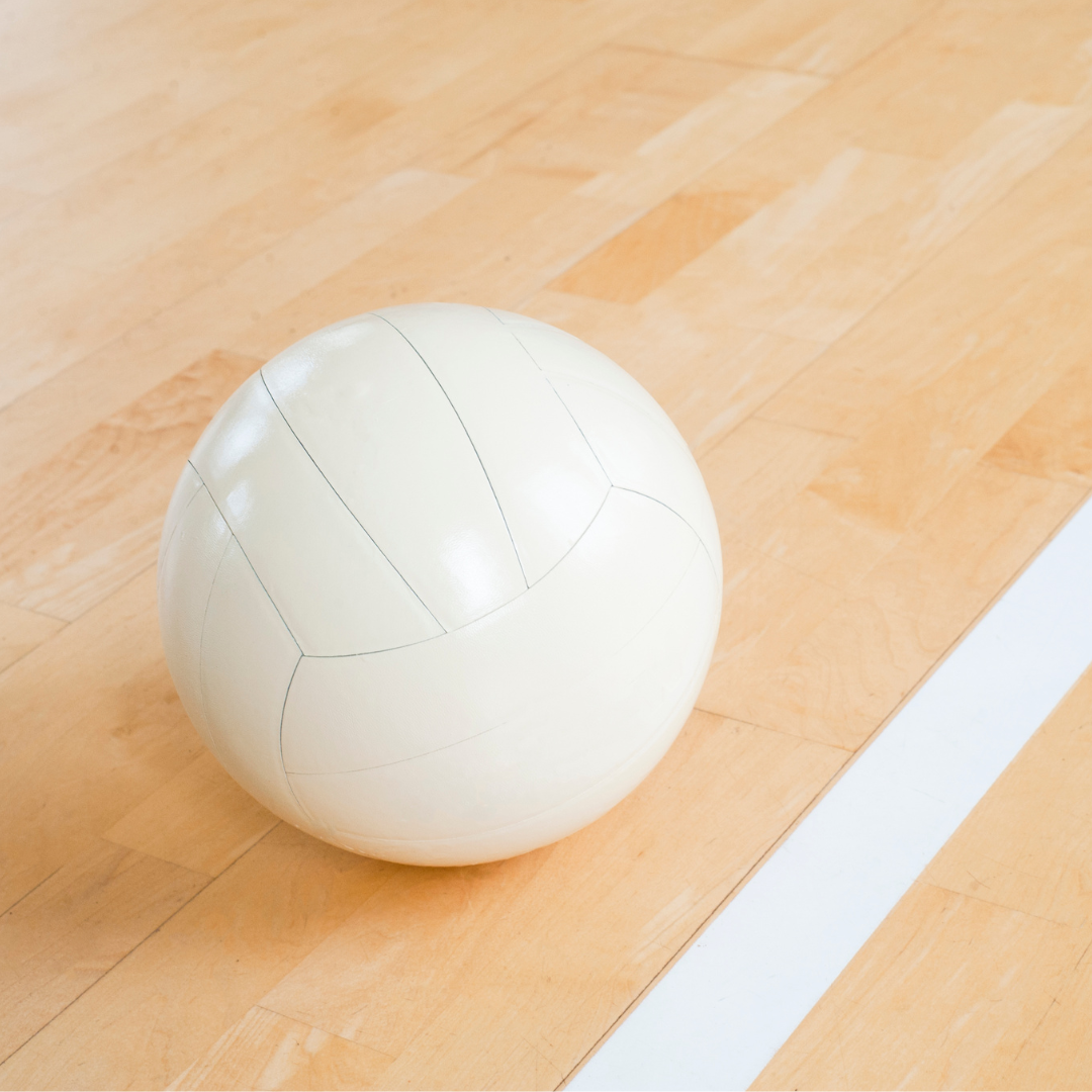 A white volleyball on a wooden floor near court lines.