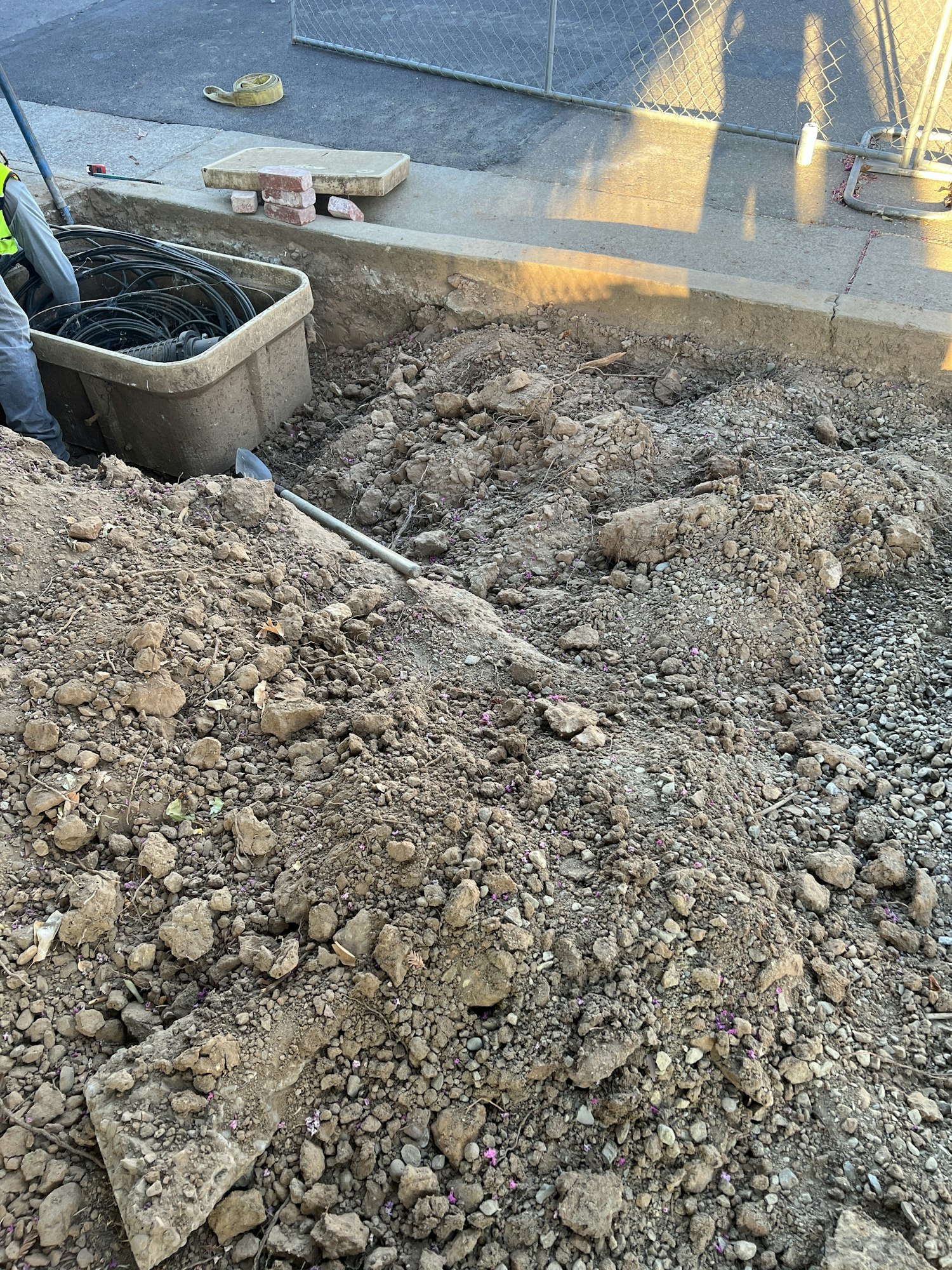 Construction site with dug-up dirt, a plastic bin of cables, and a worker partially visible.
