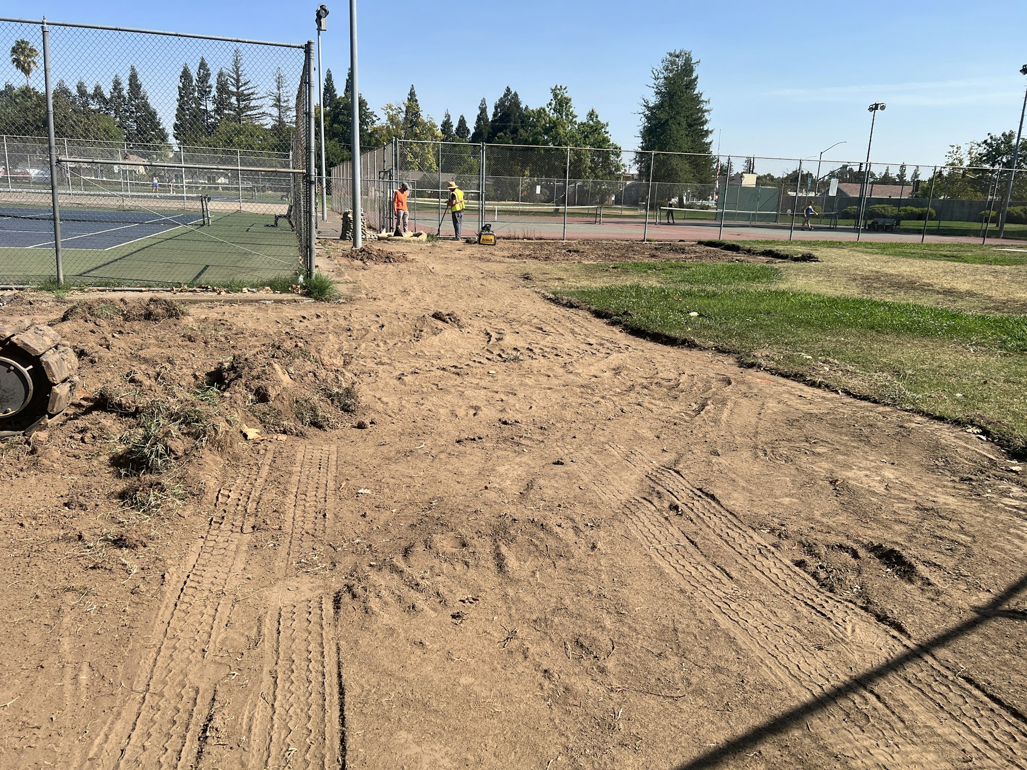 Construction work near tennis courts, with workers visible in the background.