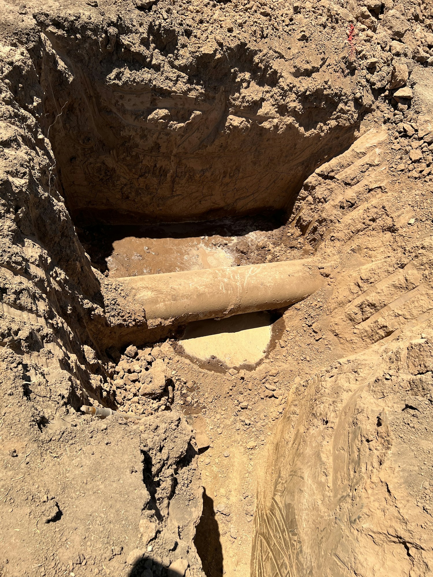 A partially exposed underground pipe surrounded by soil in a dug trench.