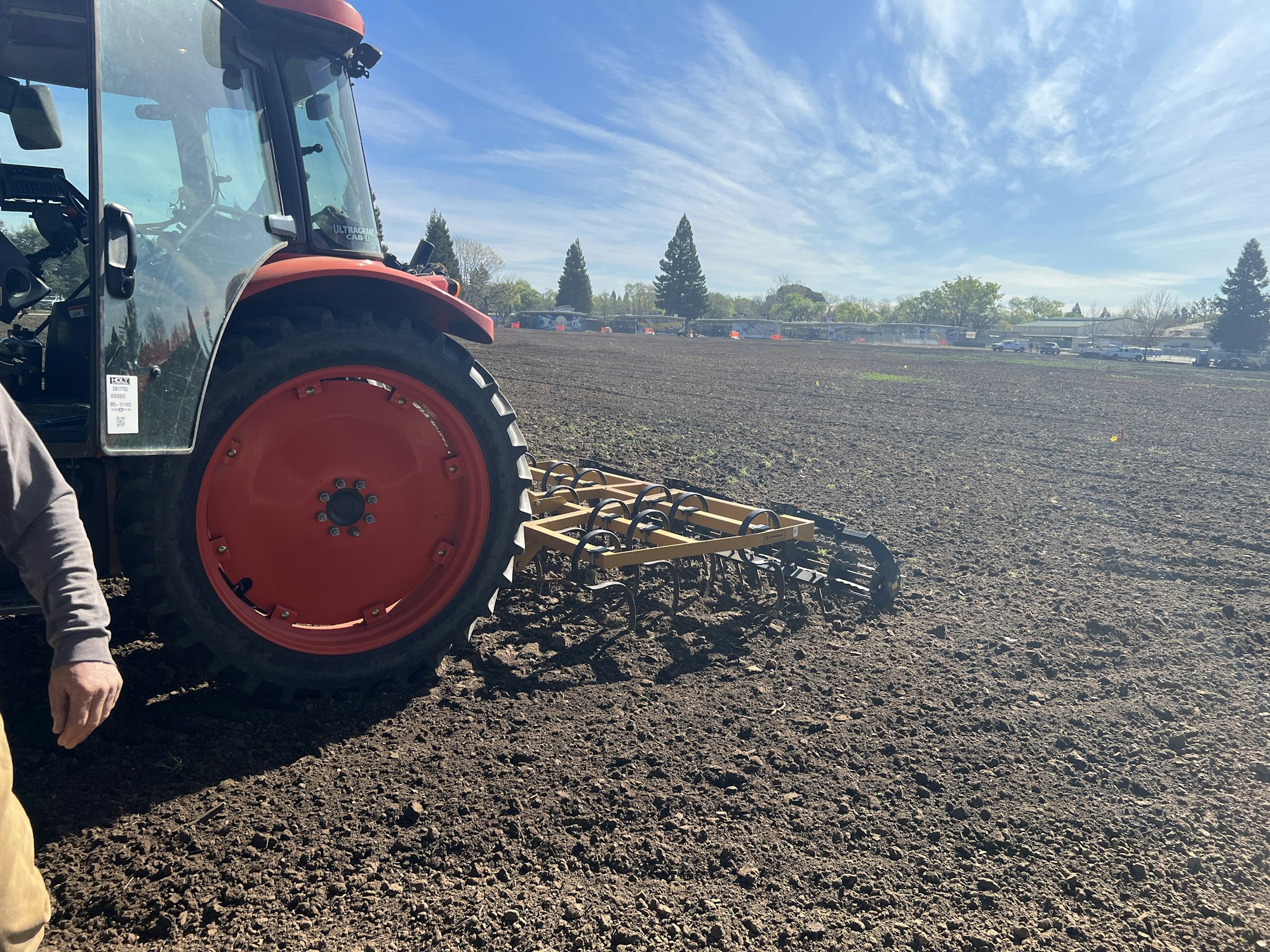 A tractor with a cultivator attachment is working in a freshly plowed field under a clear blue sky.