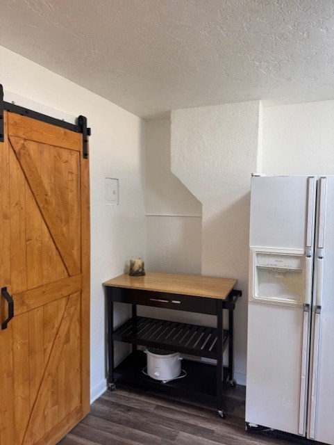 A white kitchen with a wooden barn door, a white fridge, and a rolling cart with a small appliance and a candle.