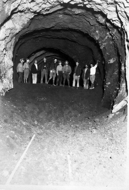 The image shows a group of men standing inside a dark mine tunnel, showcasing mining activity from the past.
