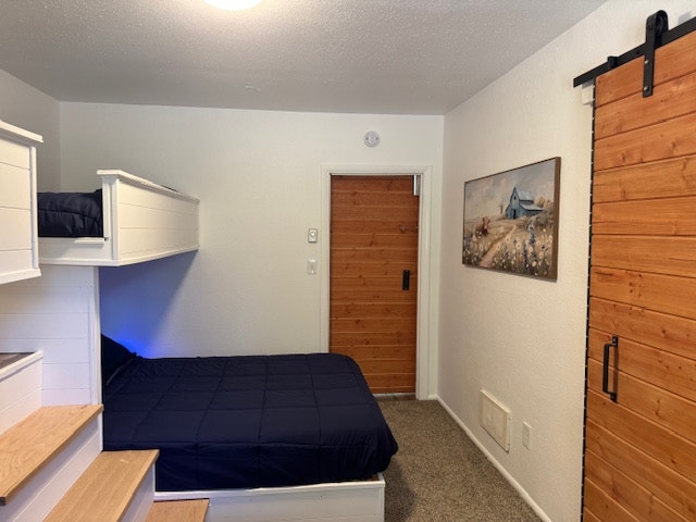 Bedroom with bunk bed, wooden barn door, stairs, framed artwork, and cozy lighting.