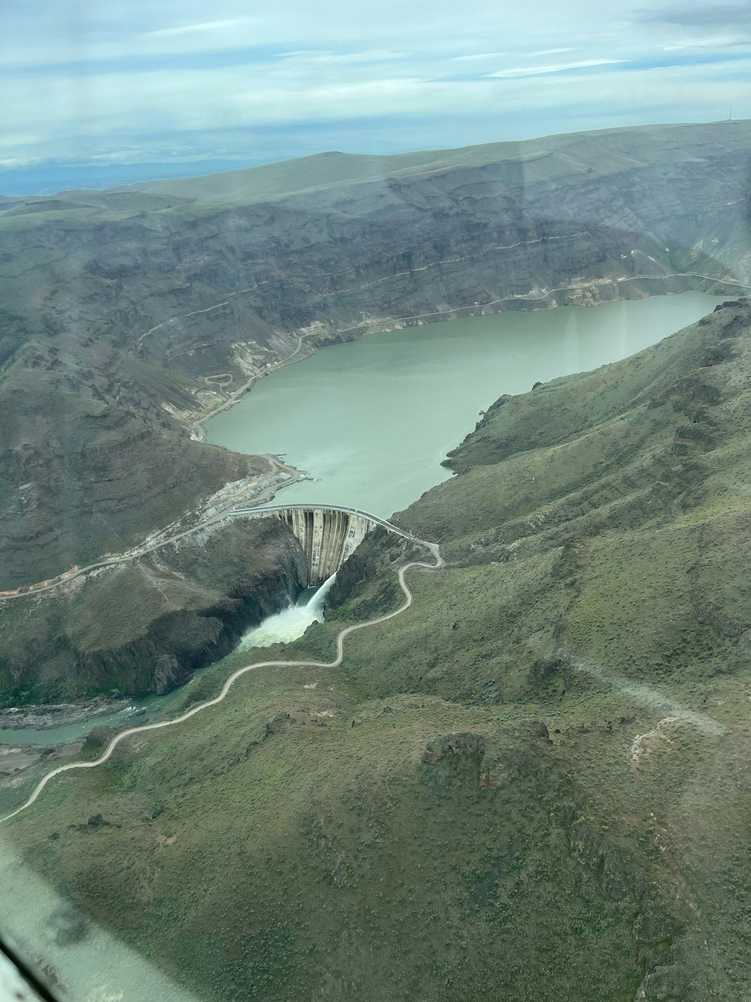 Aerial view of a dam with a reservoir, spillway, and surrounding rugged terrain.