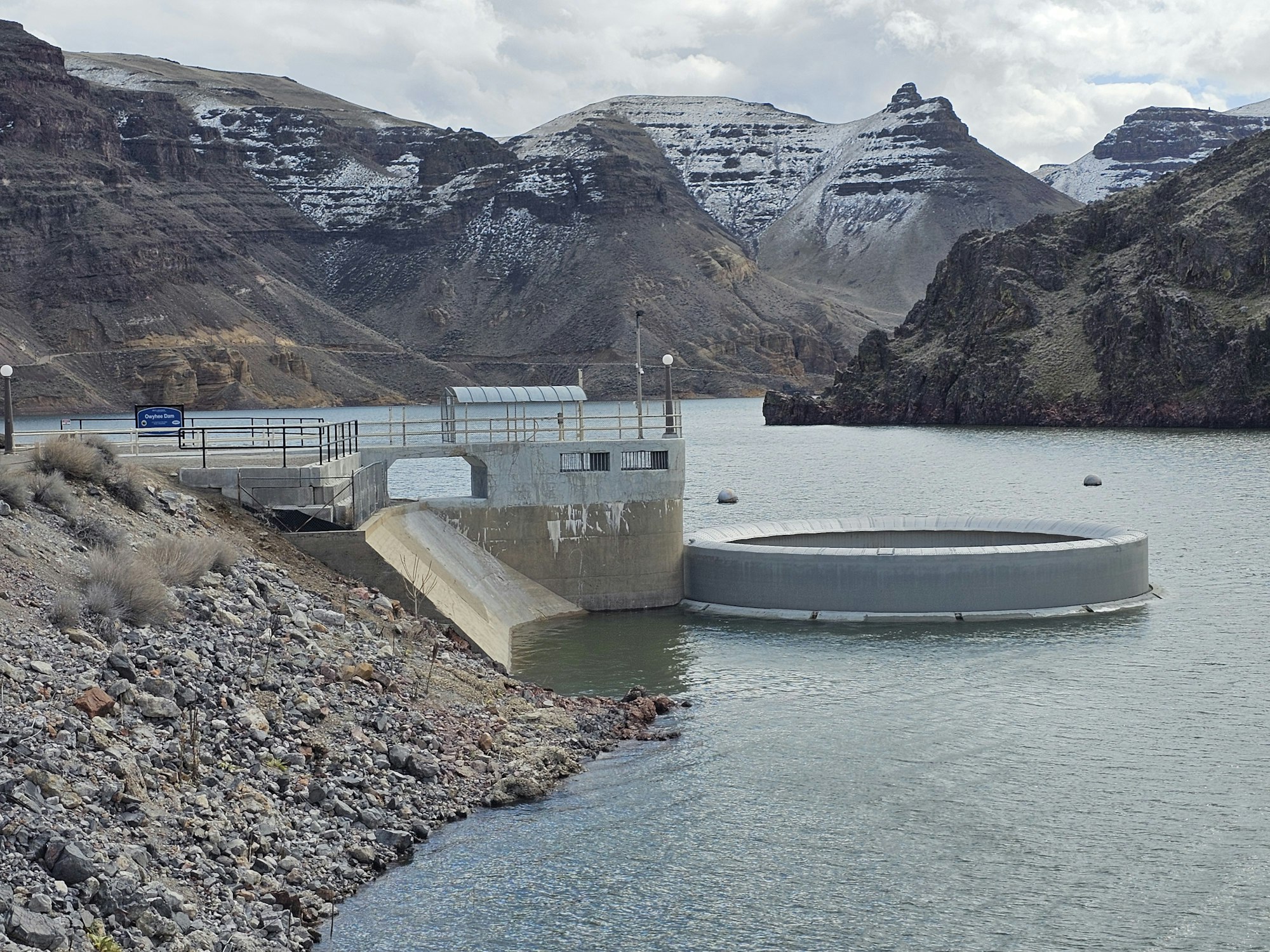 A dam intake structure on a river with snow-dusted hills in the background.