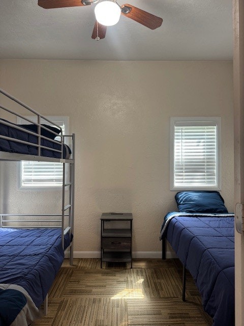 A room with a bunk bed and a single bed. Both have blue bedding. There's a small nightstand in the center and ceiling fan above.