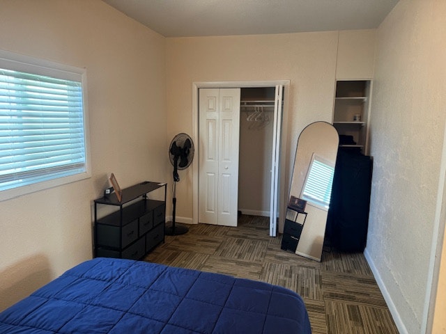 A bedroom with a bed, dresser, fan, mirror, and closet with hangers.