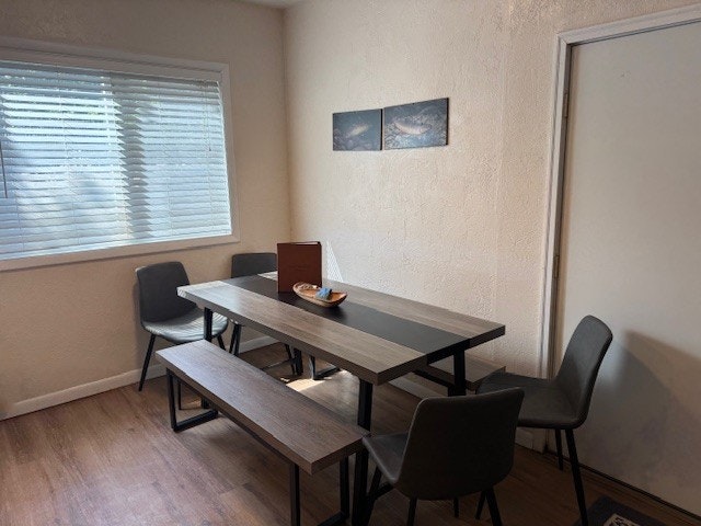 A dining area with a wooden table, benches, chairs, wall art, window blinds, and a bowl centerpiece.