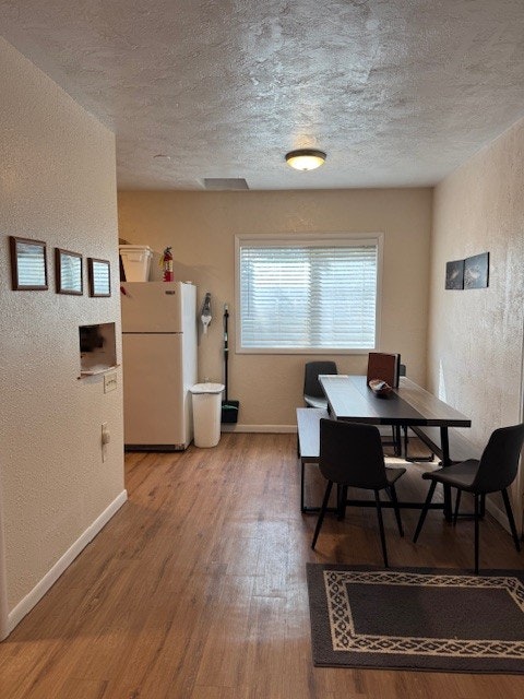 A small dining area with a table, chairs, a fridge, and wall decor.