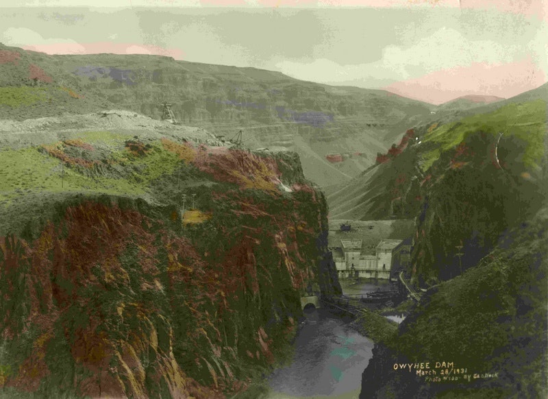 A historic, colorized image of Owyhee Dam surrounded by rugged mountains and rocky terrain, taken in 1934.