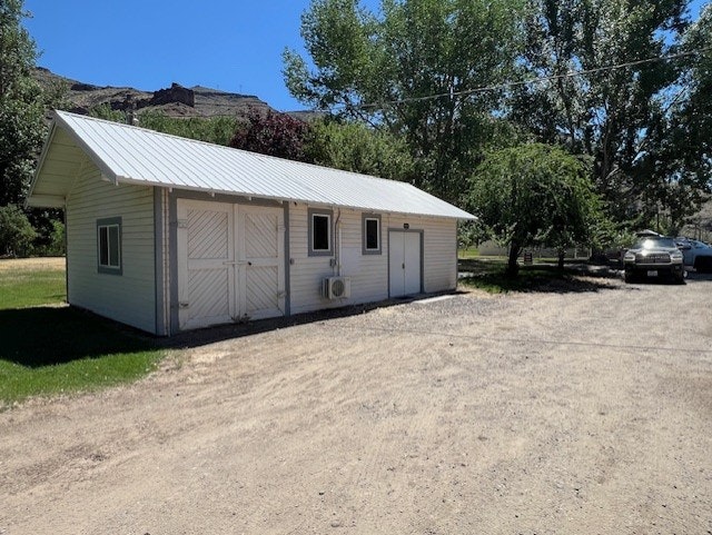 A small white building with a metal roof, surrounded by trees and parked cars on a sunny day.