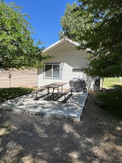 A small white house with a shaded concrete patio, picnic table, and covered grill surrounded by trees.