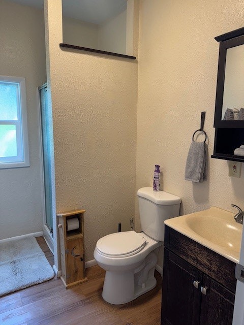 A bathroom with a toilet, sink, shower, towel on a ring, and toiletries. Wood floors and a small window are visible.