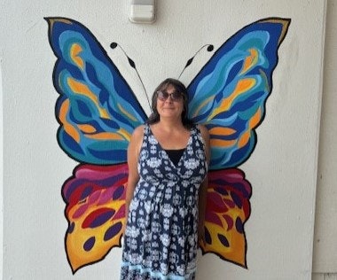 A person stands in front of a colorful butterfly wing mural, creating the illusion of having butterfly wings.