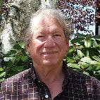 A smiling person outdoors with trees in the background.