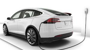 A white electric sedan car charging from a wall connector.