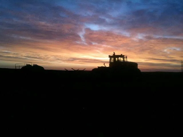 A silhouette of a tractor against a colorful sunset sky, creating a dramatic and serene landscape.