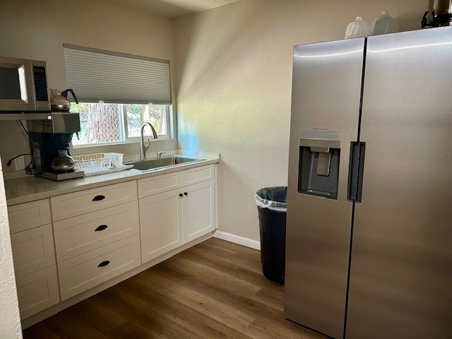 A kitchen corner with a fridge, cabinets, a sink, a microwave, a coffee maker, and a trash can.