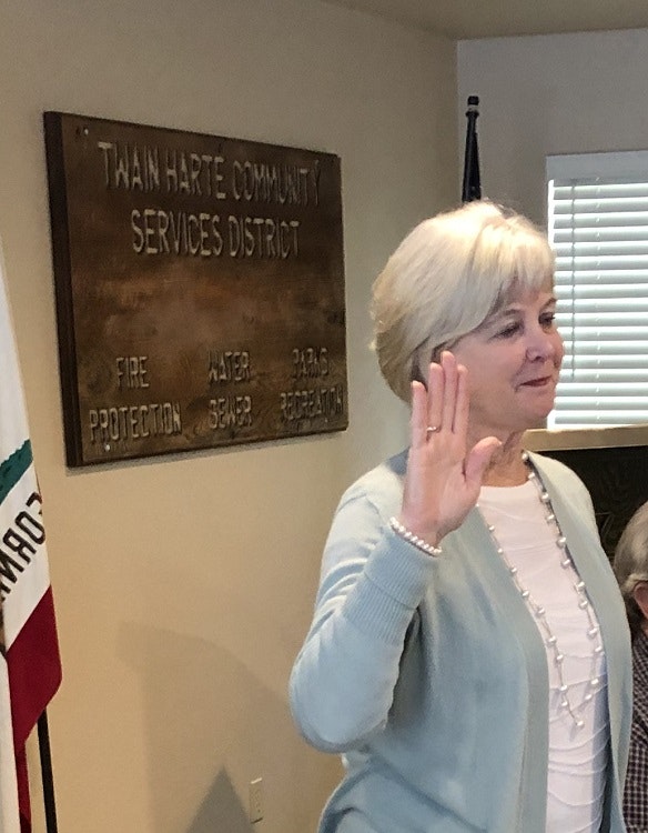 A woman is taking an oath in front of a sign for the Twain Harte Community Services District.