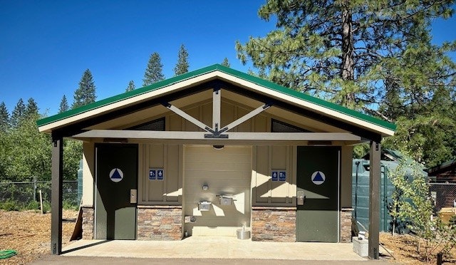 A public restroom building with separate entrances for men and women, surrounded by trees under a clear blue sky.