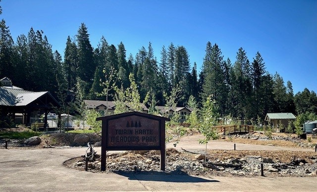 A sign for "Tuolumne Meadows Park" with trees and buildings in the background under a clear blue sky.