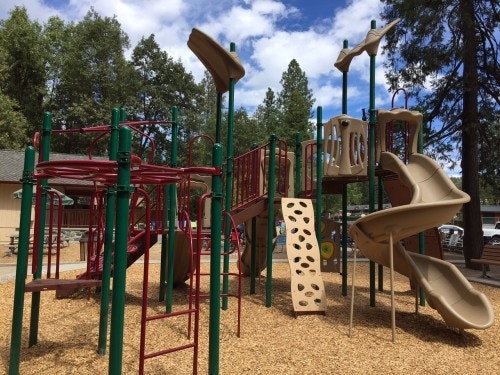 Colorful children's playground with slides, climbing frames, and a wood chip safety surface.