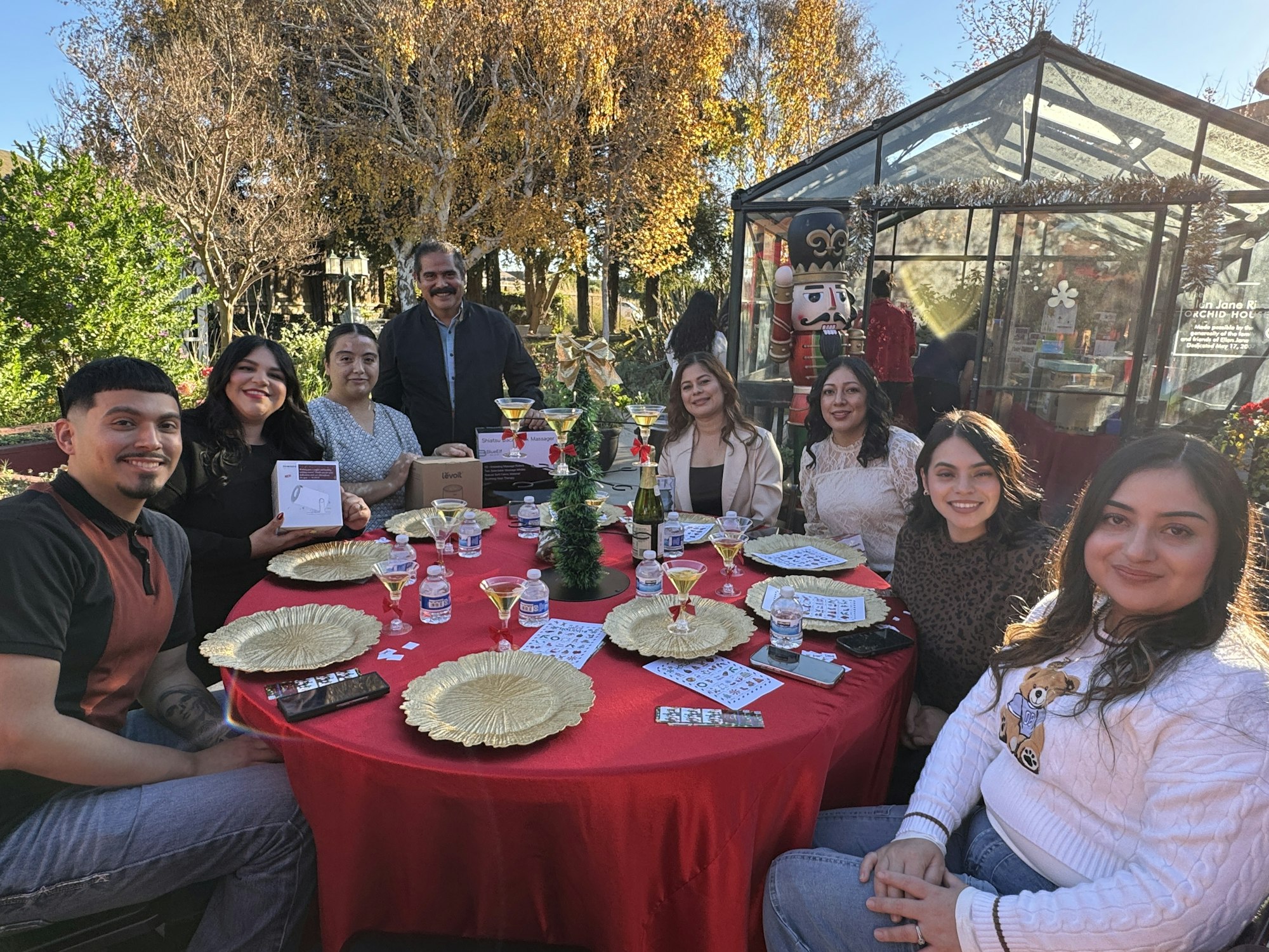 A festive gathering around a table with people, drinks, and holiday decorations in a cheerful outdoor setting.