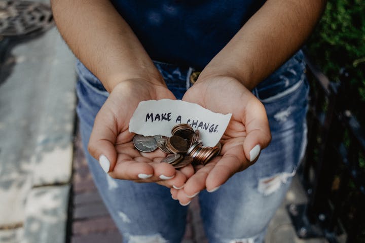 A person holds coins in their hands, with a note saying "MAKE A CHANGE" positioned above the coins.