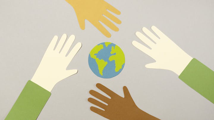 Cut-out hands of different colors reaching toward a representation of Earth on a gray background, symbolizing unity and care.