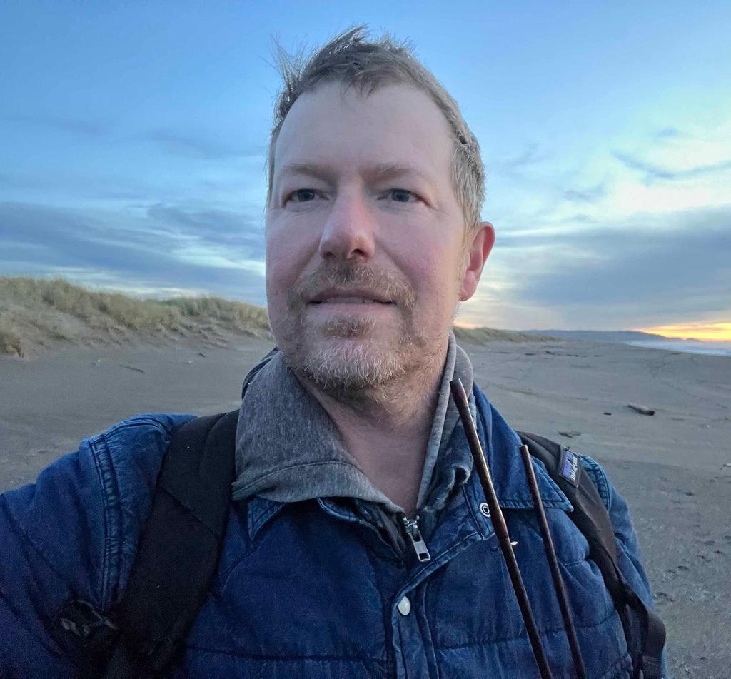A man taking a selfie on a beach at twilight.