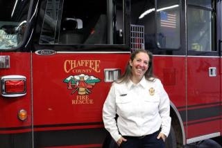 A smiling fire department official stands in front of a red fire truck, showcasing the "Chaffee County Fire Rescue" logo.