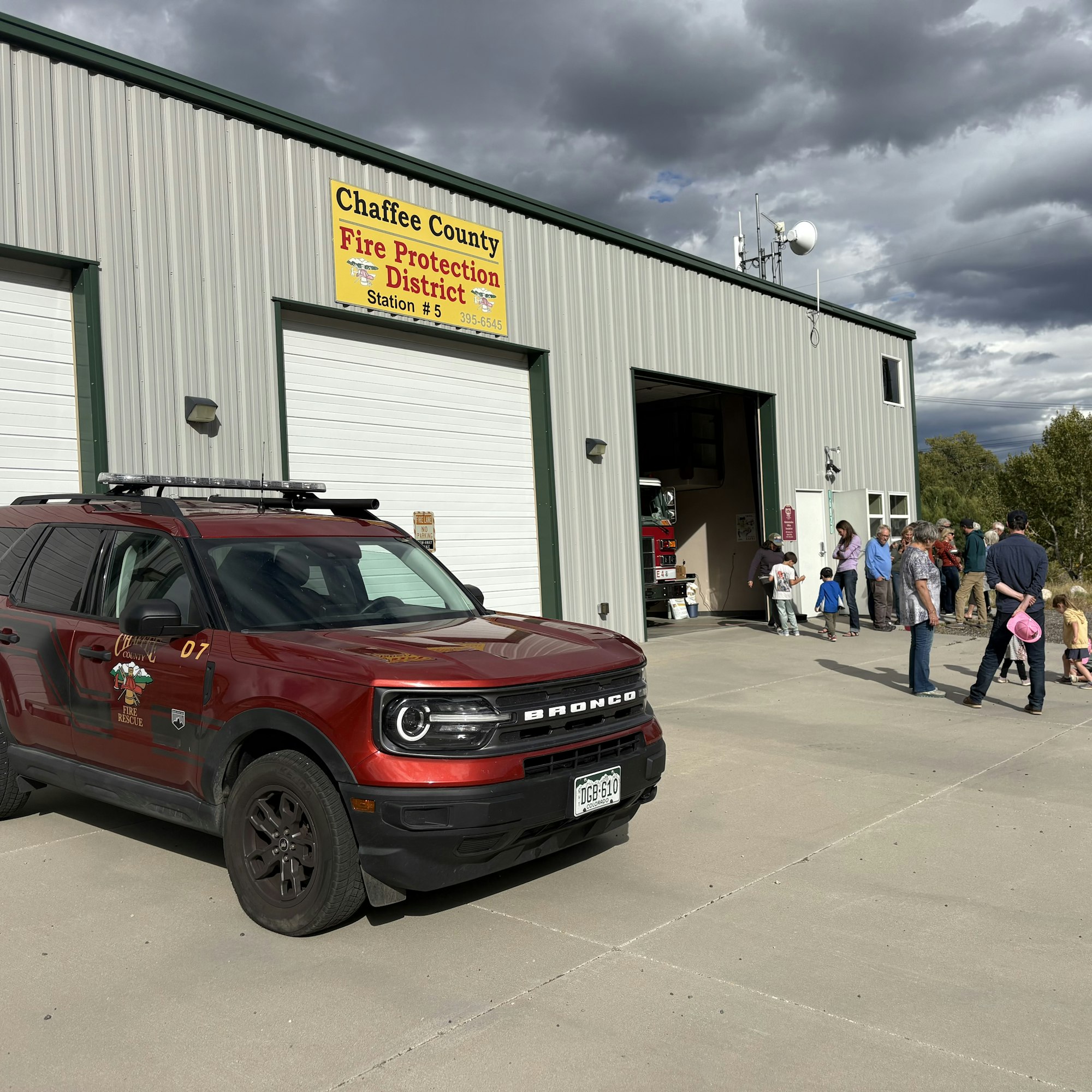 A red Bronco vehicle parked outside Chaffee County Fire Protection District Station #5, with people gathered nearby.
