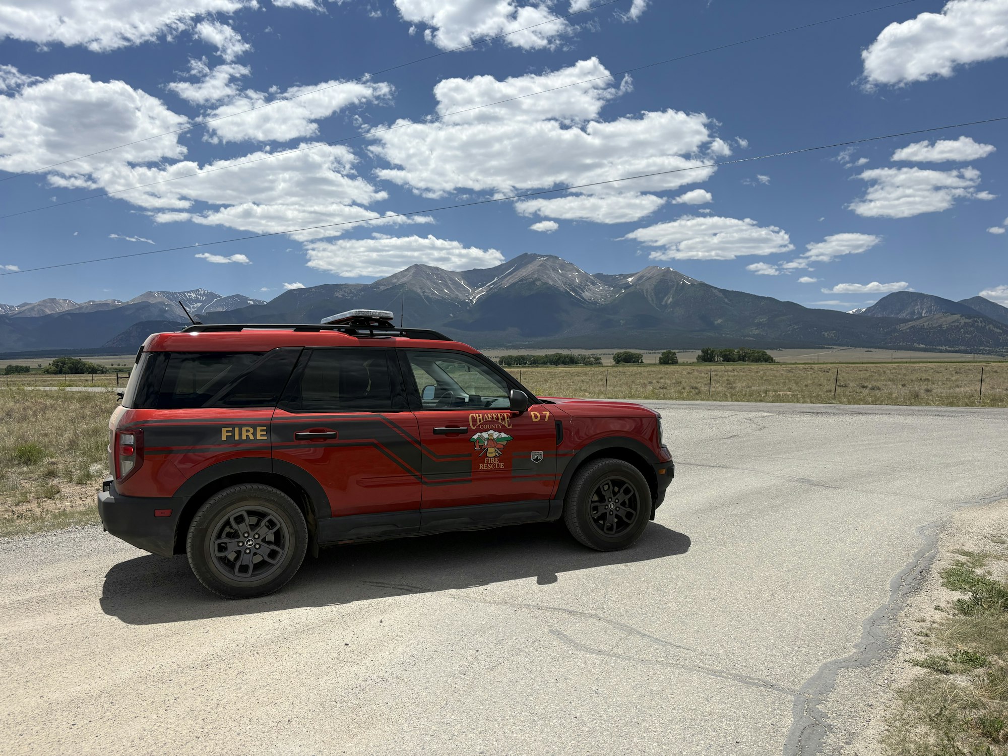 A red fire rescue vehicle parked near a road, with mountains and a blue sky in the background.