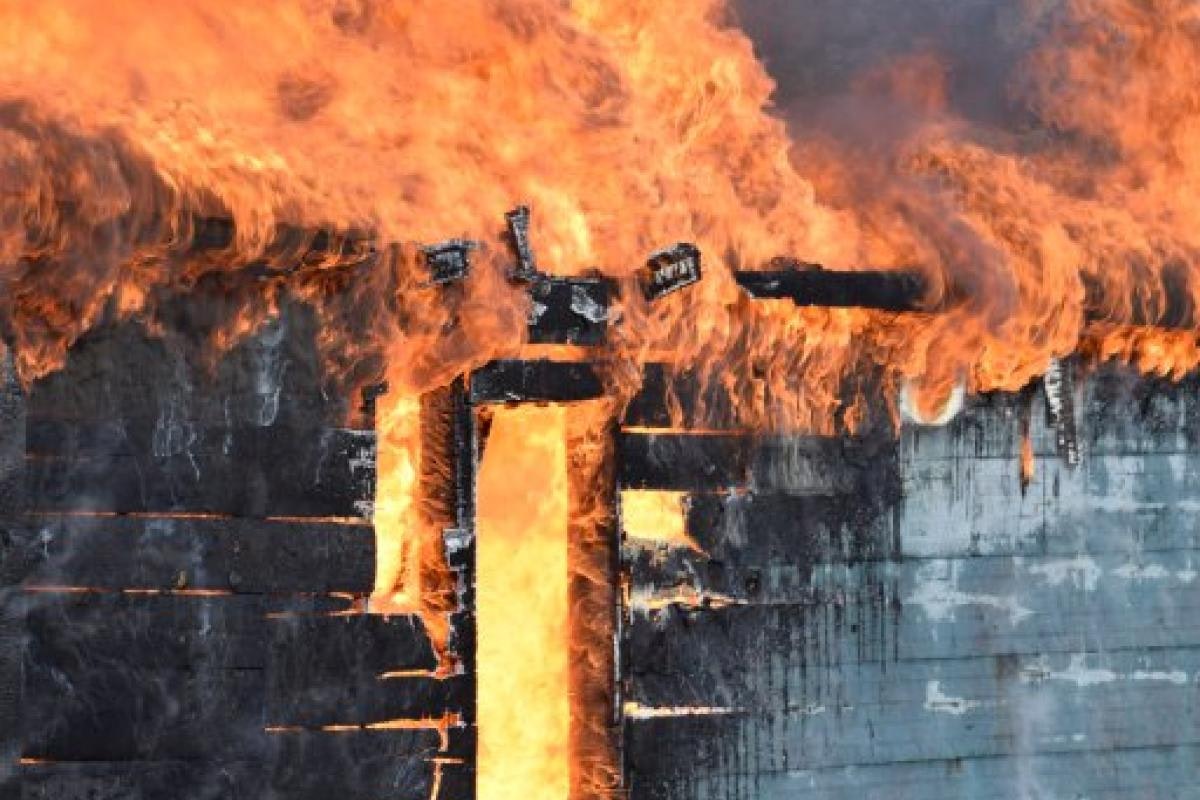 The image shows a structure engulfed in flames, with intense fire and smoke consuming the building's exterior.