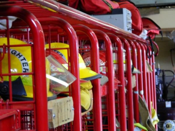 The image shows a row of fire helmets displayed on racks, with red storage compartments in the background.