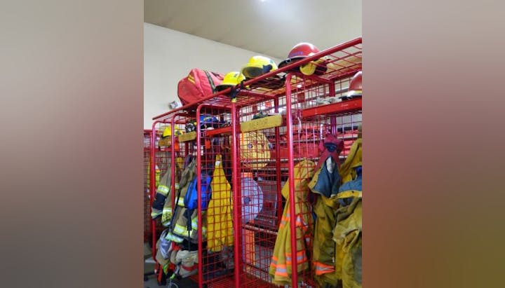 The image shows red storage racks with firefighter helmets, gear, and uniforms organized inside a fire station.
