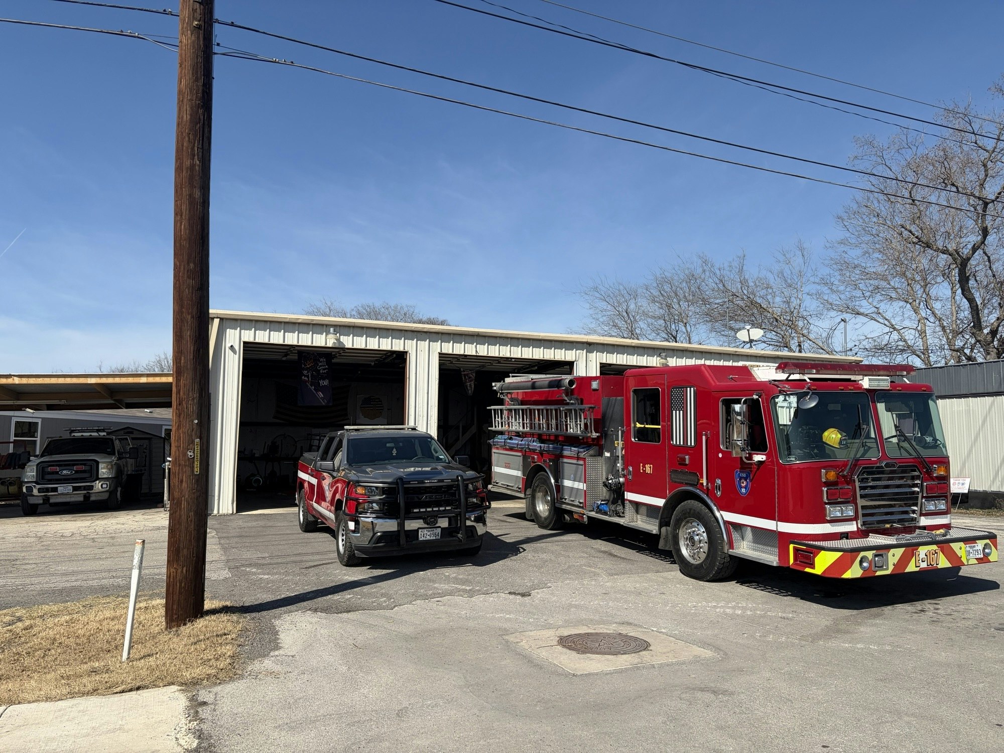 A fire truck and a pickup are parked outside a garage building, with clear blue skies overhead.
