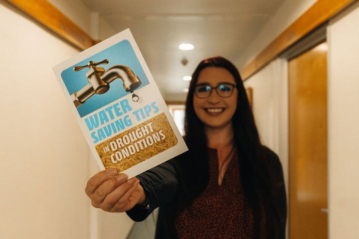 A smiling woman holding up a "Water Saving Tips in Drought Conditions" flyer.