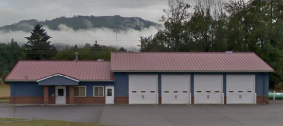 The image shows a blue and red building with several garage doors, set against a backdrop of misty mountains.