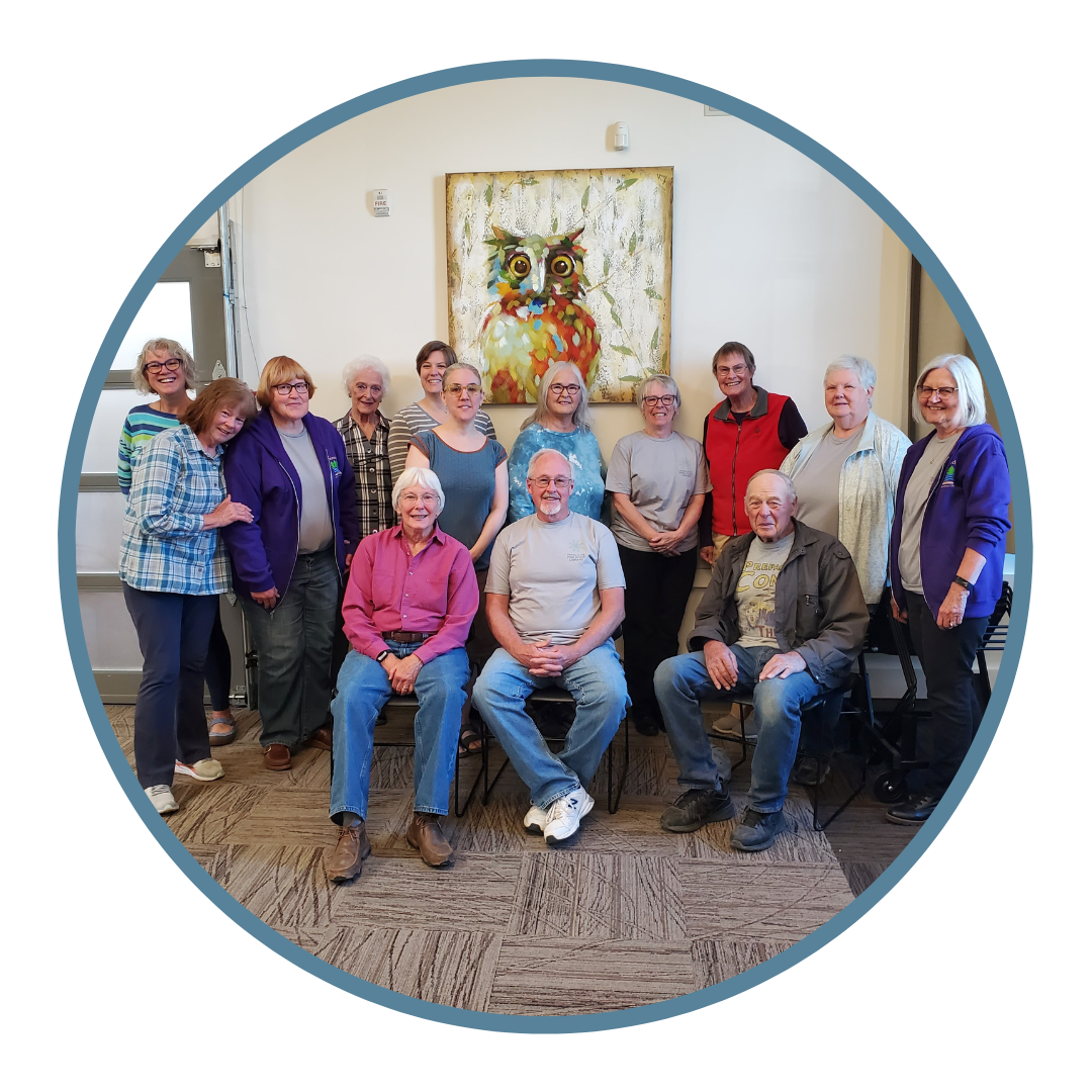 A group of smiling people posing for a photo with an owl painting in the background.