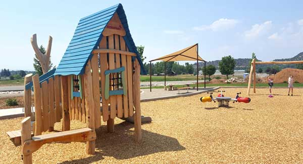 Playground with wooden playhouse, swings, and a seesaw on a sunny day.