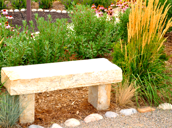 A stone bench surrounded by lush greenery and colorful flowers in a tranquil garden setting.