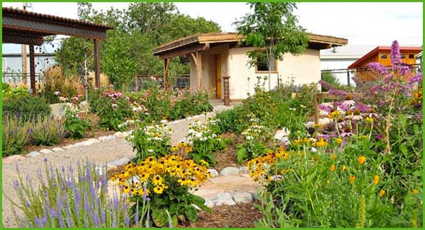 A colorful garden with flowers, a pathway, and a small building with a brown roof under a cloudy sky.