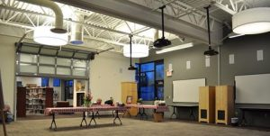 Empty modern room with tables, chairs, bookshelves, and large overhead lights.