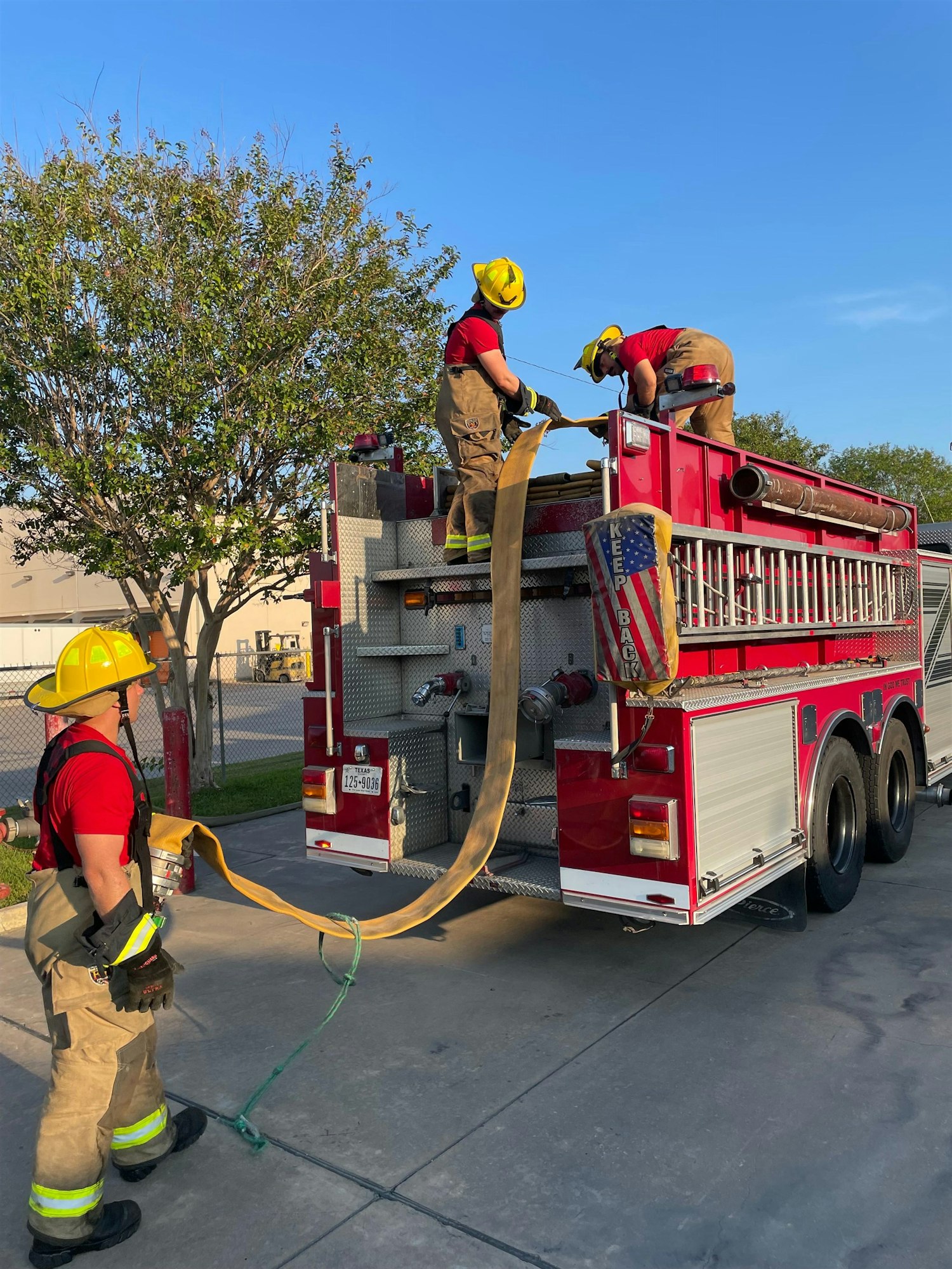 Firefighters are preparing equipment on a fire truck, handling hoses under a clear blue sky.