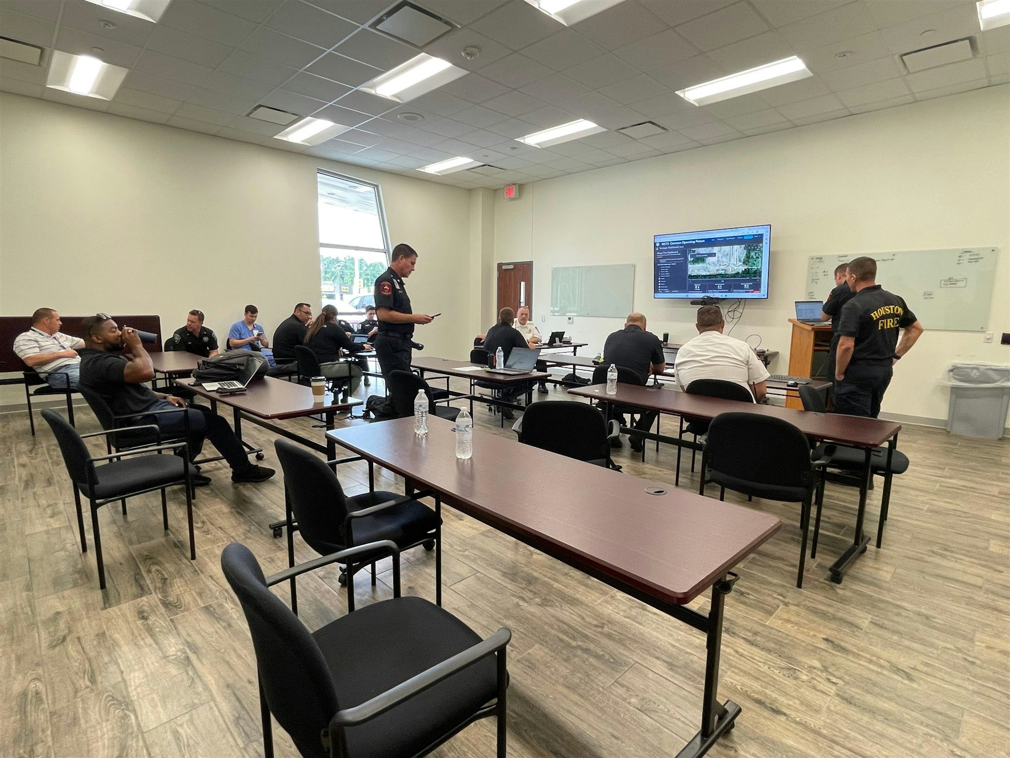 A group of people is attending a meeting in a classroom setting, likely discussing operational matters with a presentation displayed.